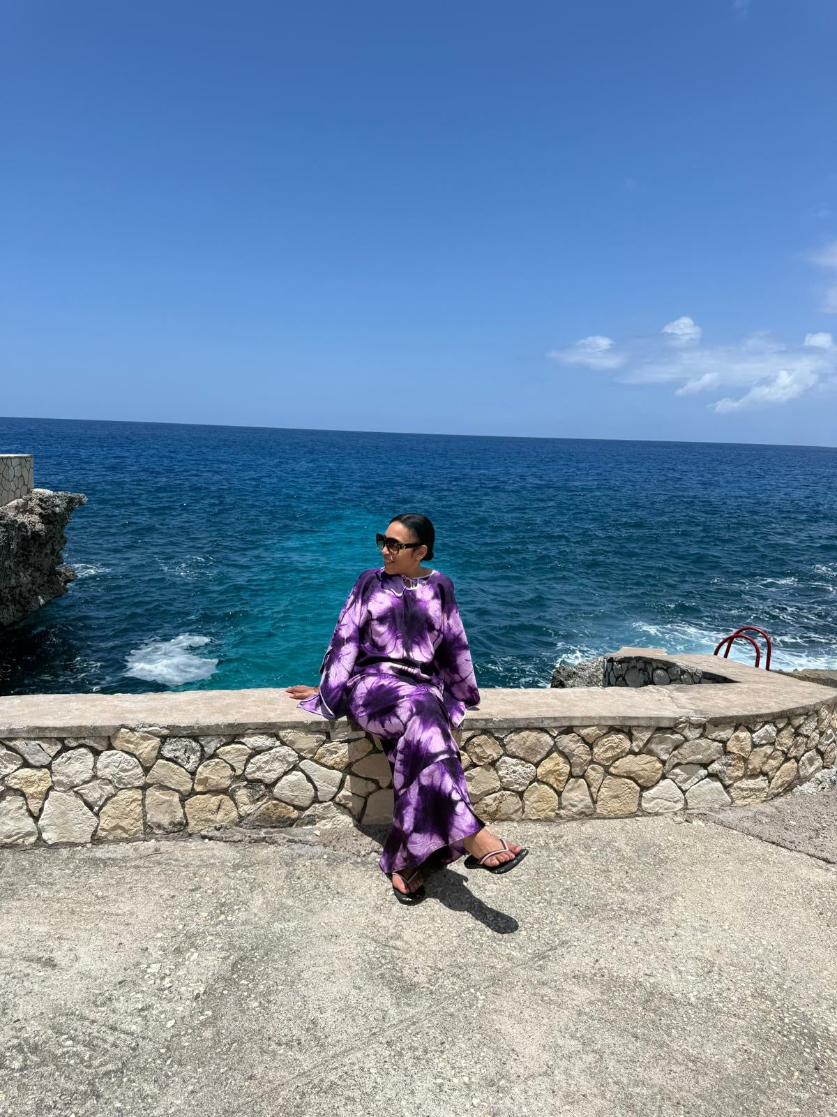 The Indigo Tide Caftan in deep violet tie-dye, worn oceanside